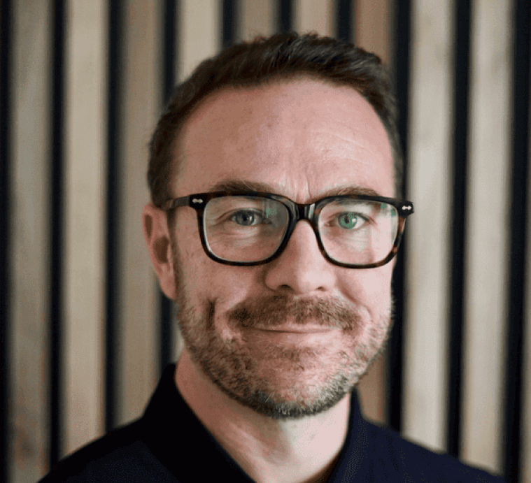 Headshot of a smiling man with dark hair, glasses, and a beard looking directly at the camera.